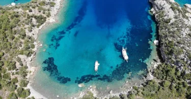 Datça Akvaryum Koyu havadan panoramik görünümü ve turkuaz denizde süzülen tekneler.