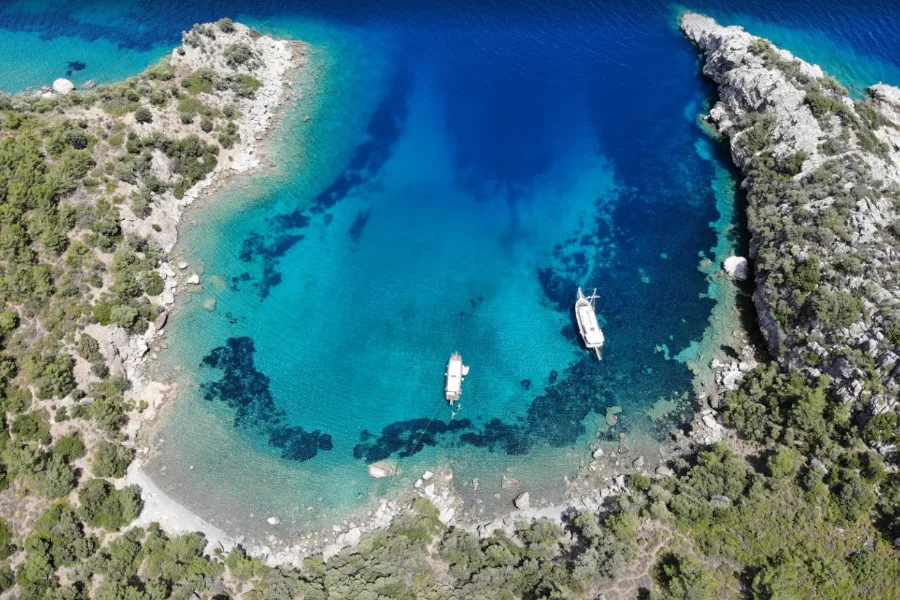 Datça Akvaryum Koyu havadan panoramik görünümü ve turkuaz denizde süzülen tekneler.